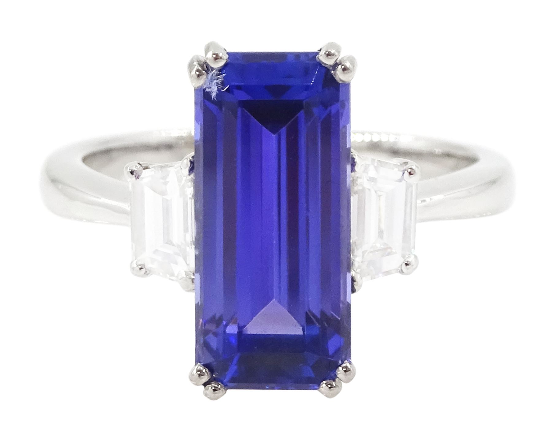 Platinum tanzanite and diamond three stone ring, single emerald cut tanzanite of approx 4.20 carat, with with a single trapeze cut diamond set either side, stamped PT950, total diamond weight approx 0.49 carat, with Alan Poultney Gems report