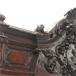 Large and impressive 19th century heavily carved mahogany display cabinet, the ornate pediment carved with a central scalloped and foliate rocaille motif with extending acanthus leaves and egg-and-dart moulding flanked by acanthi finials, over a central cartouche with carved bow-and-arrow motif and trailing scrollwork, the bookcase enclosed by two glazed doors with bevelled glass sides, the base with a gadrooned upper edge over a central rocaille ornament with scrolling acanthus leaves, the panelled frieze with further foliate motifs, raised on large carved snarling lion mask supports with floral garlands and claw feet, united by a concave rectangular platform base with gadrooning egg-and-dart moulding
