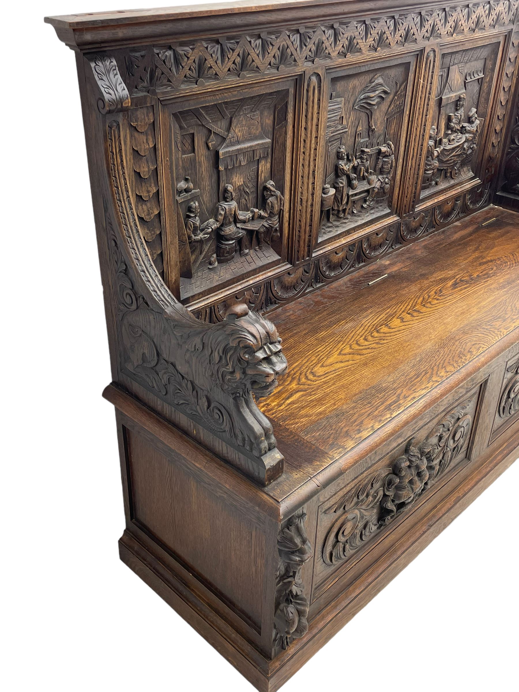 19th century heavily carved oak settle, the moulded upper rail over triangular foliage carved frieze, three Flemish style carved panels depicting tavern scenes, acanthus carved uprights terminating to lion carved arms, hinged box seat, the panelled front carved with lion masks and extending scrolled acanthus leaves, on moulded skirt base