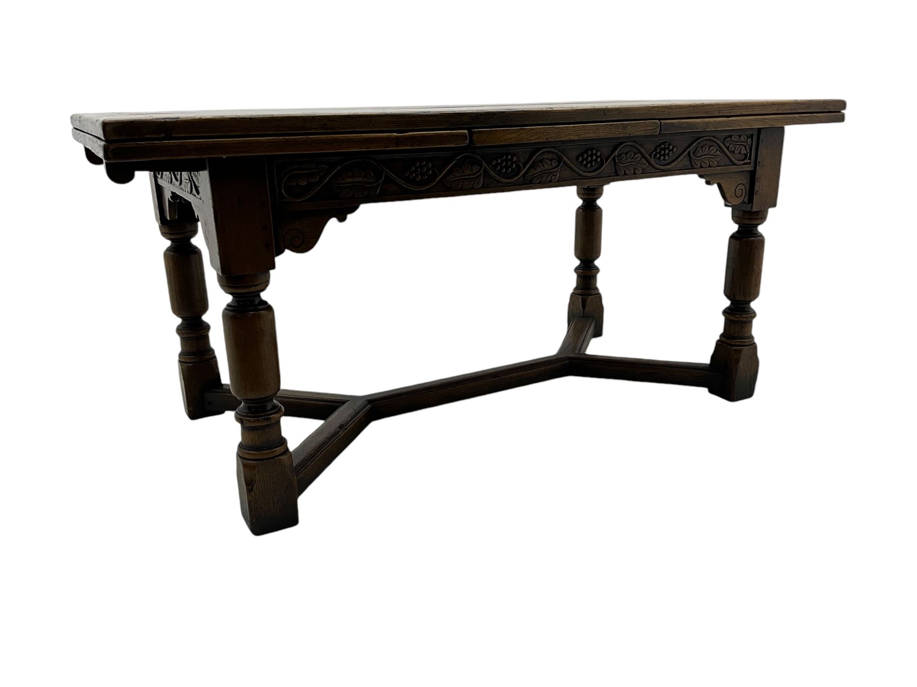 Early 20th century Jacobean design draw-leaf oak dining table, rectangular top with carved frieze depicting scrolling foliage and grape clusters, sliding extending leaves, raised on robust turned supports united by H-stretcher  