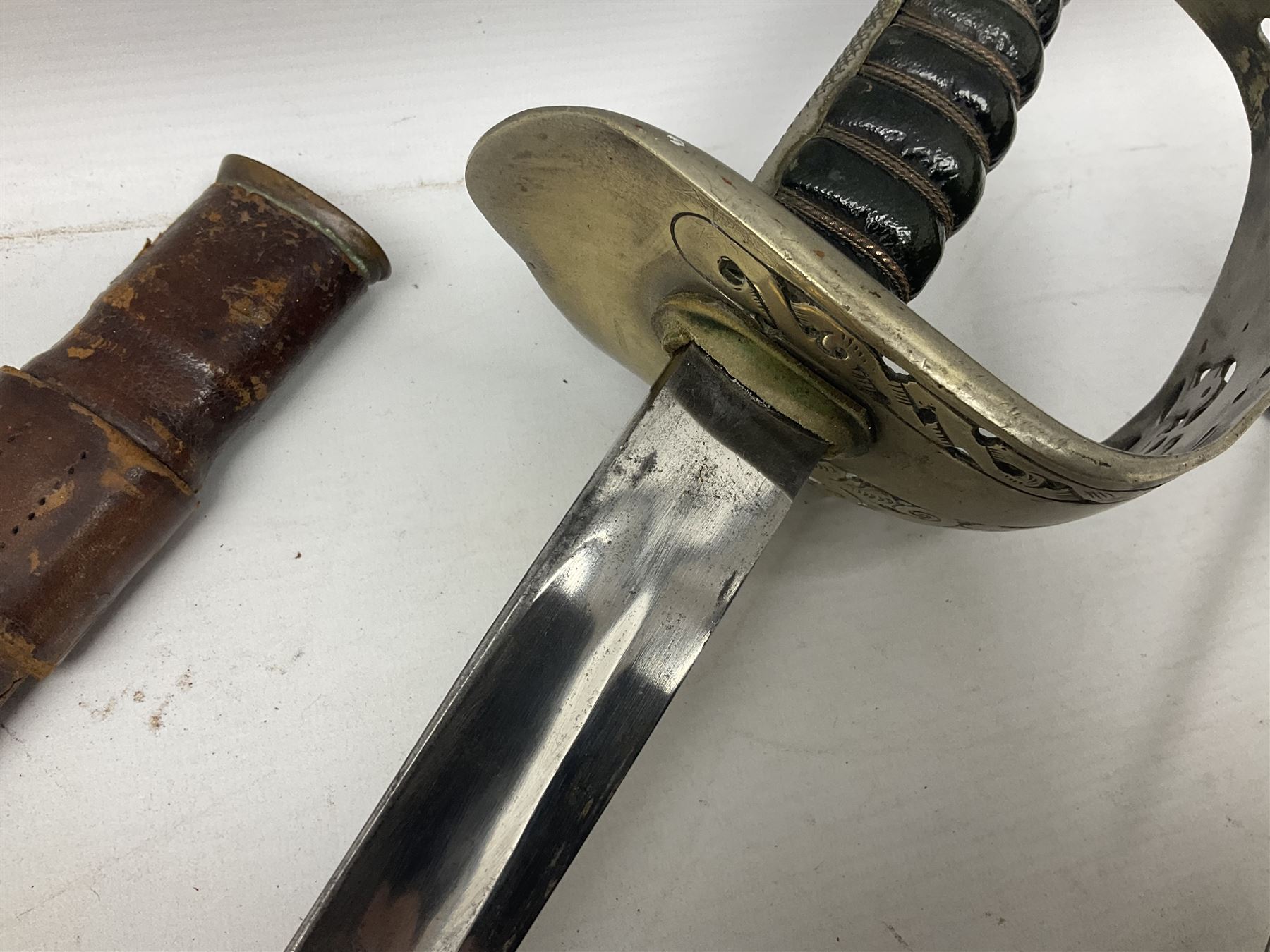 George V British Army 1897 pattern officers sword with plain 82cm fullered steel blade, pierced  basket hilt with George V cypher and wire bound leather grip with chequered backstrap; in leather covered field service scabbard L101cm overall; and another officer's sword in relic condition lacking scabbard (2)