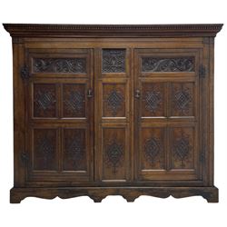 Large 18th century and later oak livery cupboard, projecting moulded and dentil cornice, sunken fillet moulded frame, triple vertical panelled central upright, enclosed by two doors each with five panels, the top row of panels carved with stylised scrolls, the lower panels carved with foliate lozenges, on shaped bracketed skirt base 
