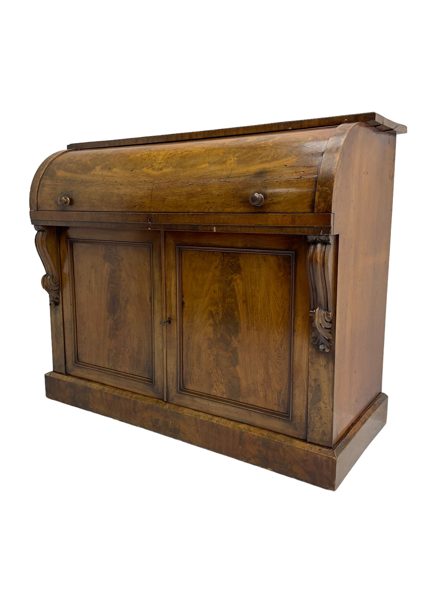 Victorian mahogany roll-top writing desk, top concealing fitted interior with pigeonholes and three drawers, the trisector inset writing surface with writing slope, base fitted with panelled cupboard enclosing single shelf, decorated with scrolled corbels