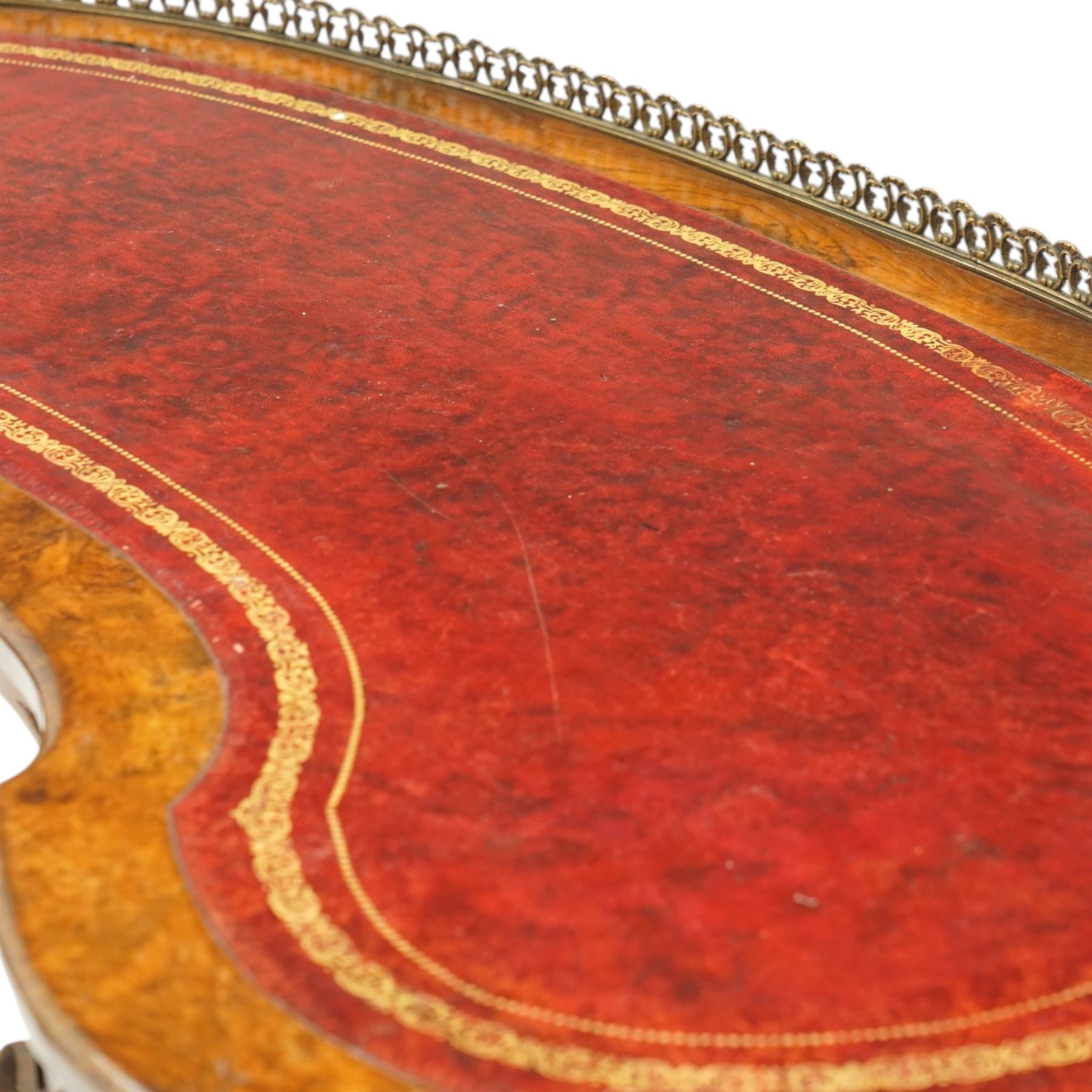 Victorian figured burr walnut kidney-shaped writing table, shaped top with pierced raised bras gallery back over inset red leather writing surface, fitted with two drawers flanking a pierced and carved scrolling apron, raised on turned and gadrooned twin pedestals with scroll-moulded cabriole supports with ceramic castors, united by ring-turned stretcher