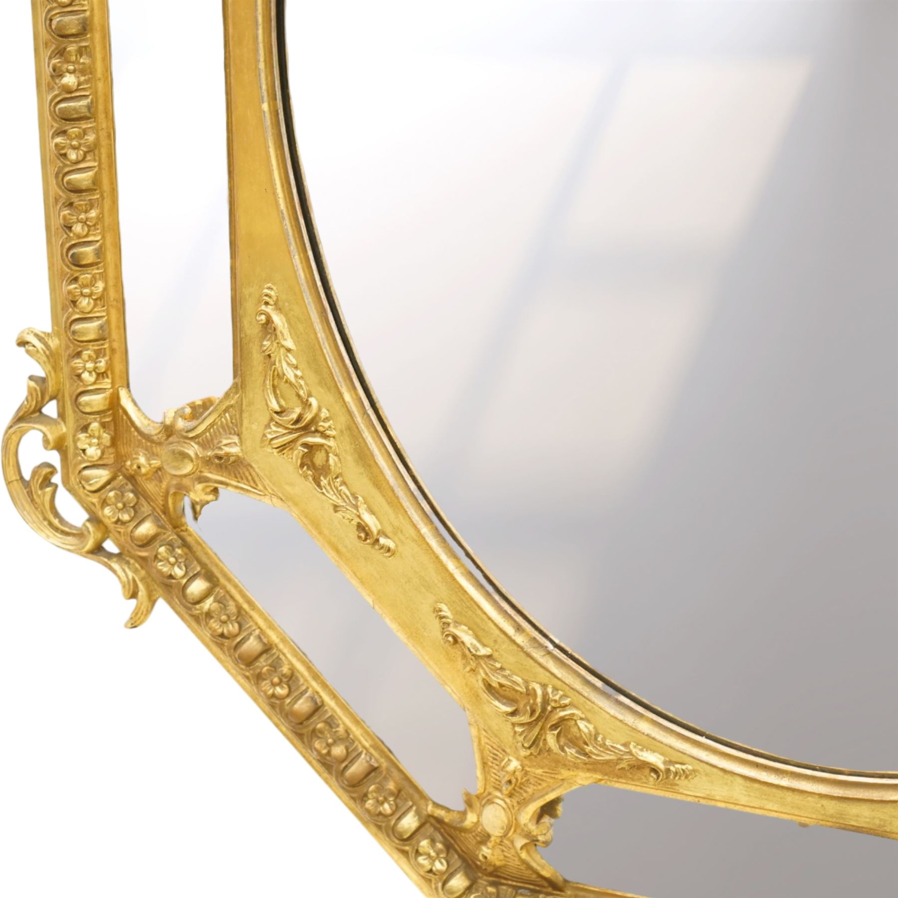 Late 19th century French giltwood and gesso wall hanging cushion mirror, the pierced foliate rocaille pediment extending acanthi C-scrolls and trailing bellflowers, over a floral garland and cartouche moulded rails, the central oval bevelled plate surrounded by further bevelled cushion mirrors, with out-scrolling pierced motifs flanking the floral egg-and-dart moulded outer edge, over a pierced foliate cartouche terminal