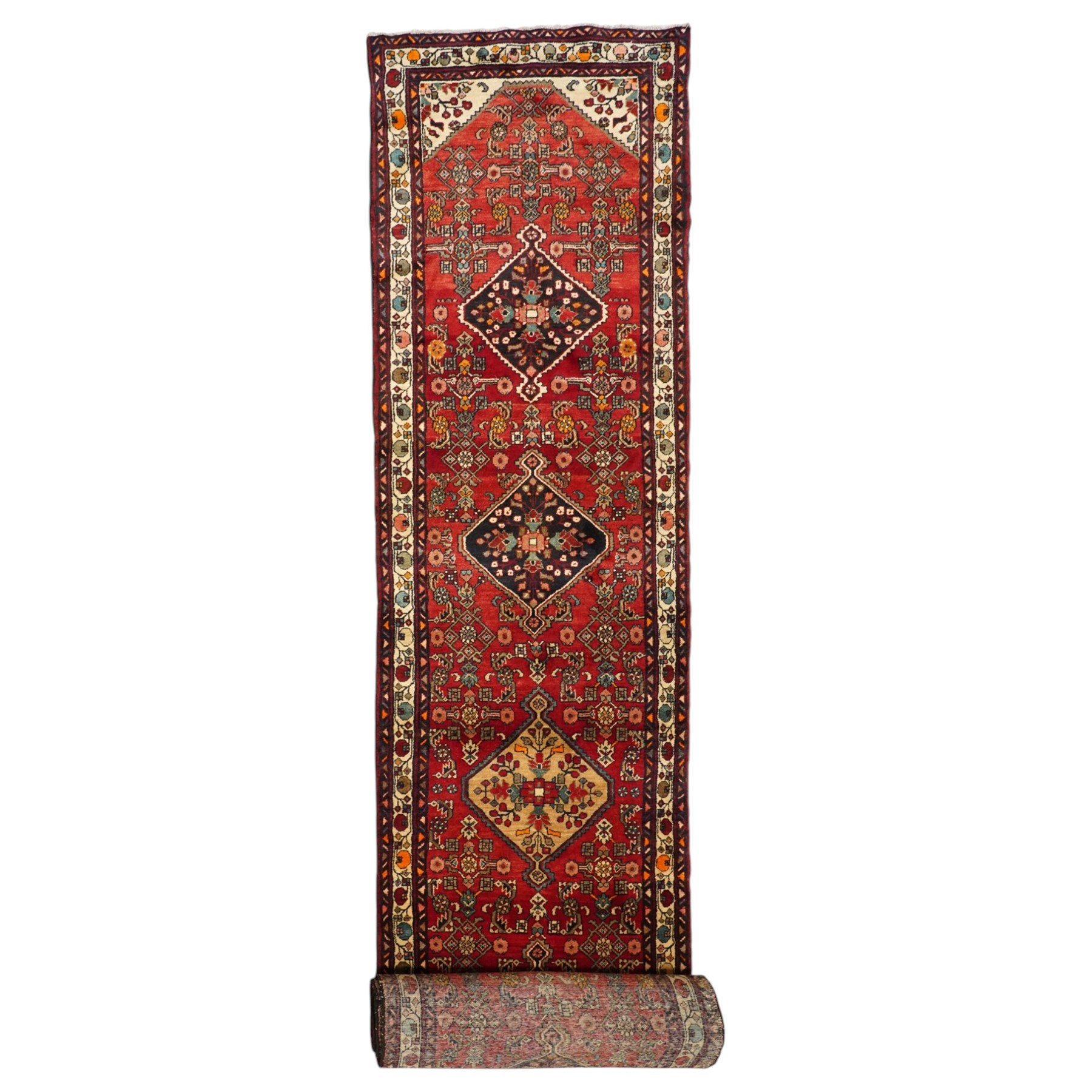 Large Persian Qashqai runner rug, the red ground decorated with navy and ivory lozenge medallions interspersed with stylised floral and geometric motifs, enclosed by an ivory flowerhead border and patterned guard stripes
