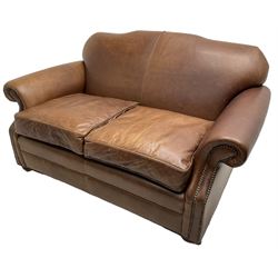 Traditional shape two-seat sofa, shaped back and rolled arms upholstered in tan leather with stud work bands, on compressed bun feet with castors 
