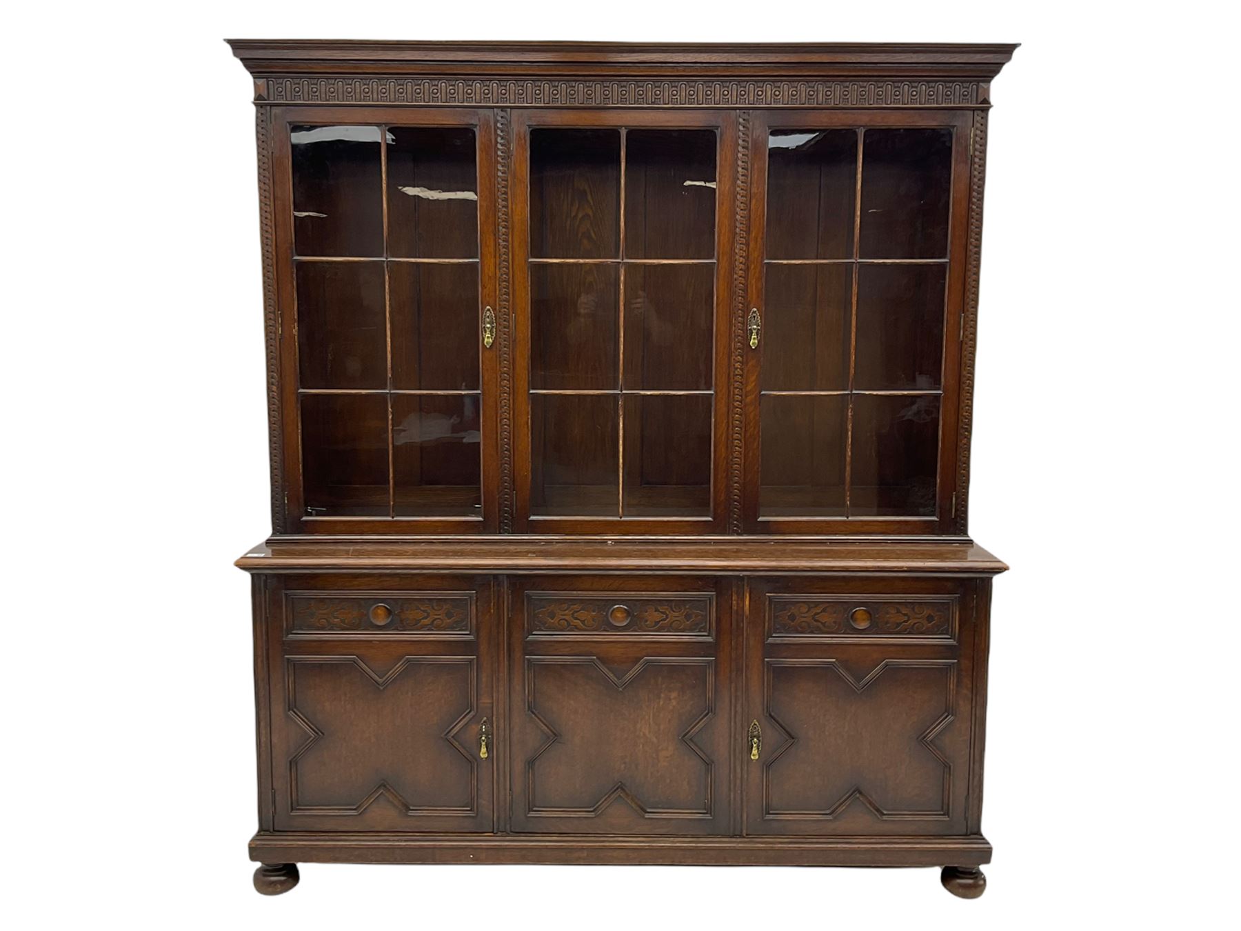 Waring and Gillow - oak bookcase on cupboard, projecting cornice over arcade frieze, guilloche upright decoration, the top section enclosed by three astragal glazed doors, the lower section enclosed by three geometric panelled doors with blind fretwork decoration, on turned feet