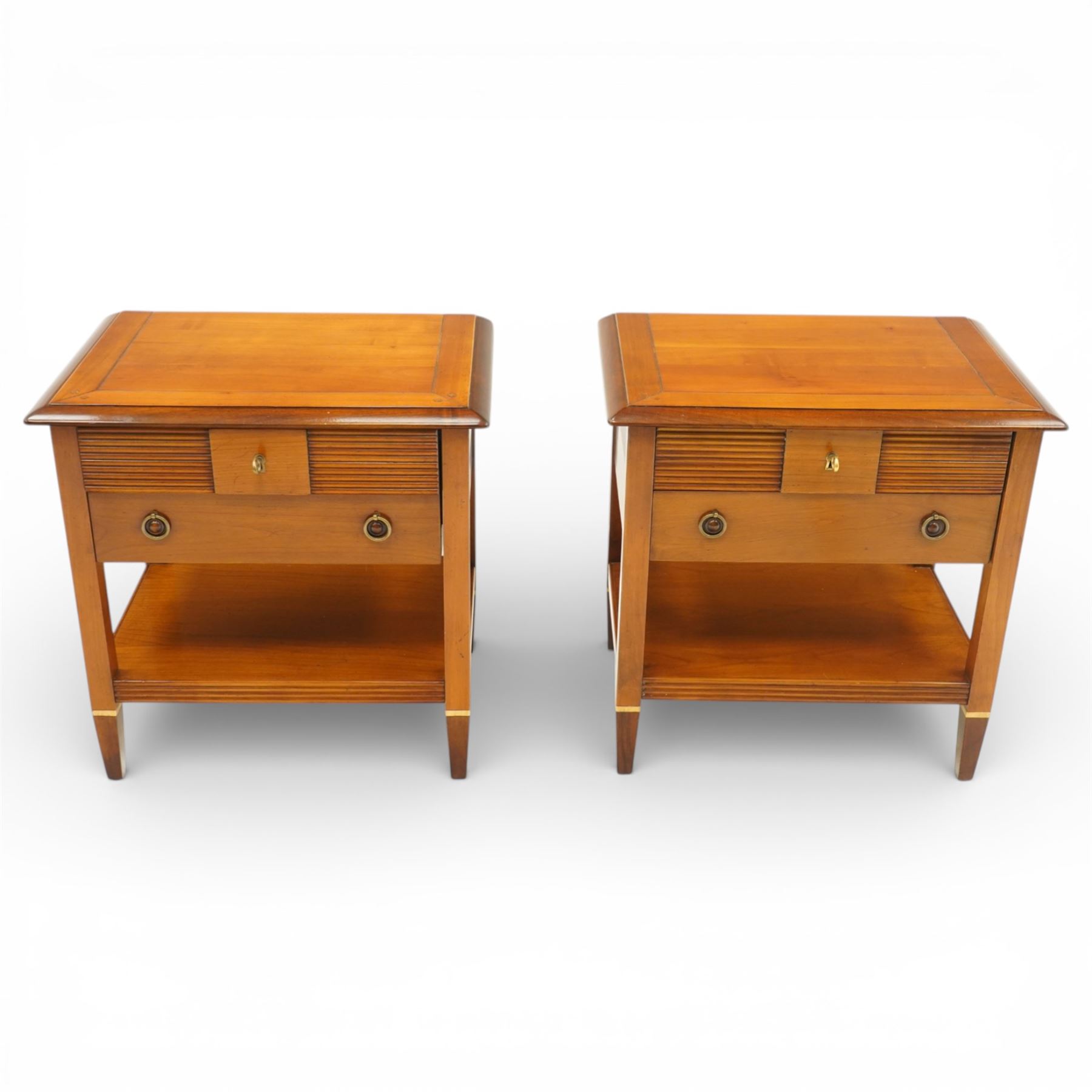 Brigitte Forestier - pair of cherry wood bedside cabinets, moulded rectangular top above two drawers, the top drawer with reeded panels flanking a brass circular pull, the lower drawer with two brass pulls, on square tapering supports united by a full length undertier