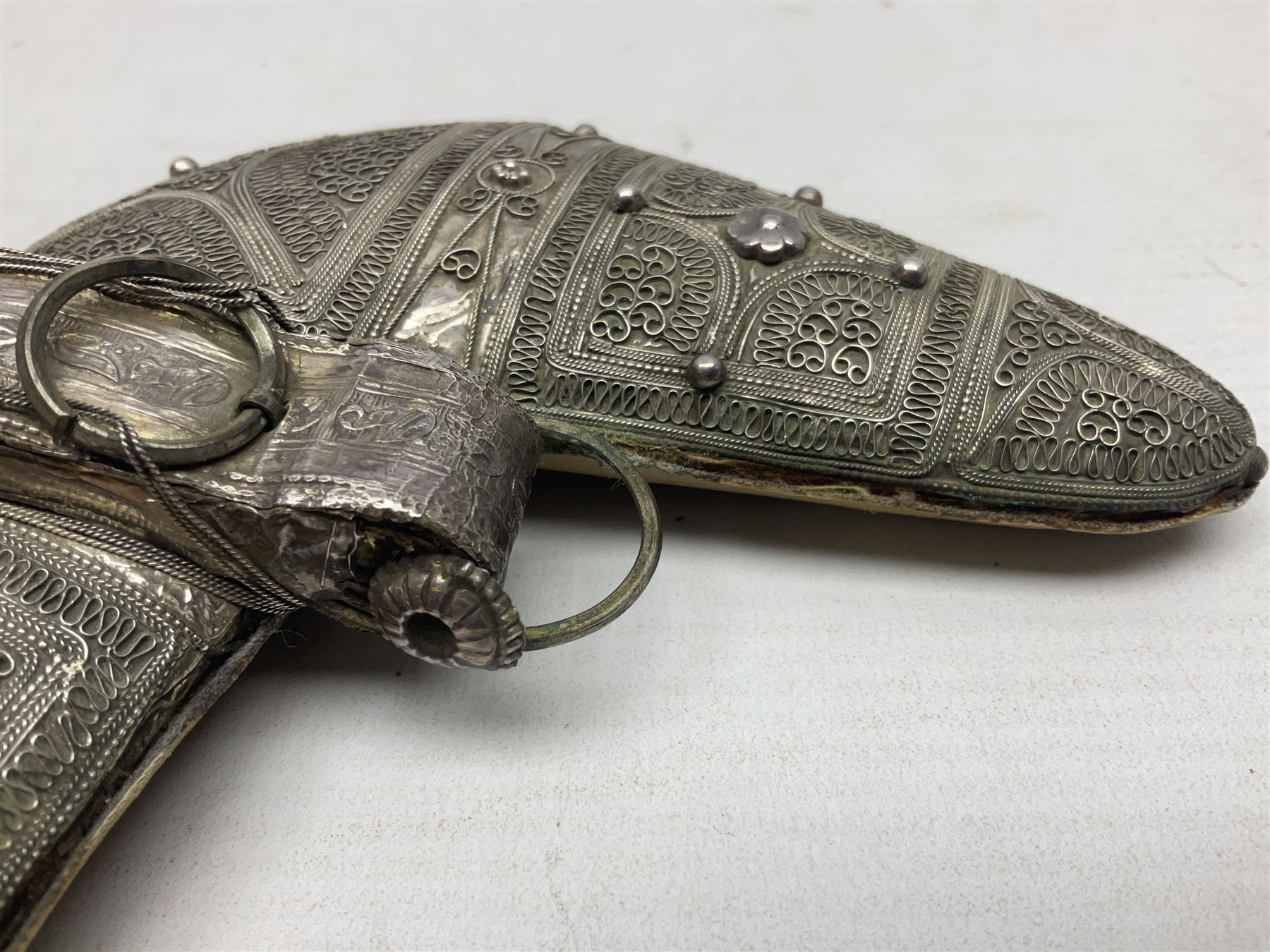 Omani Khanjar dagger, the 12.5cm curved blade with pronounced medial rib to either side, waisted horn style hilt with dome shaped pommel and inlaid pique work; in an intricately filigree decorated white metal scabbard with rings woven into the belt mount L25cm overall