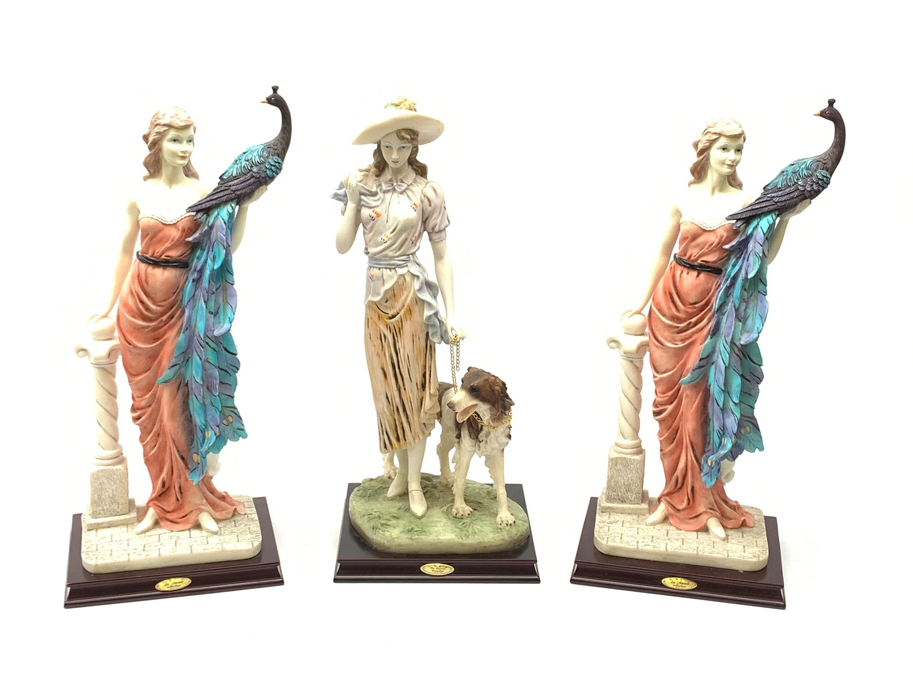  A pair of La Anina Collection figurines, each modelled as a female figure in pink dress supporting a peacock on one arm, and resting the other upon a classical column, H51.5cm, together with another similar figurine modelled as a female figure with hound at her side.   