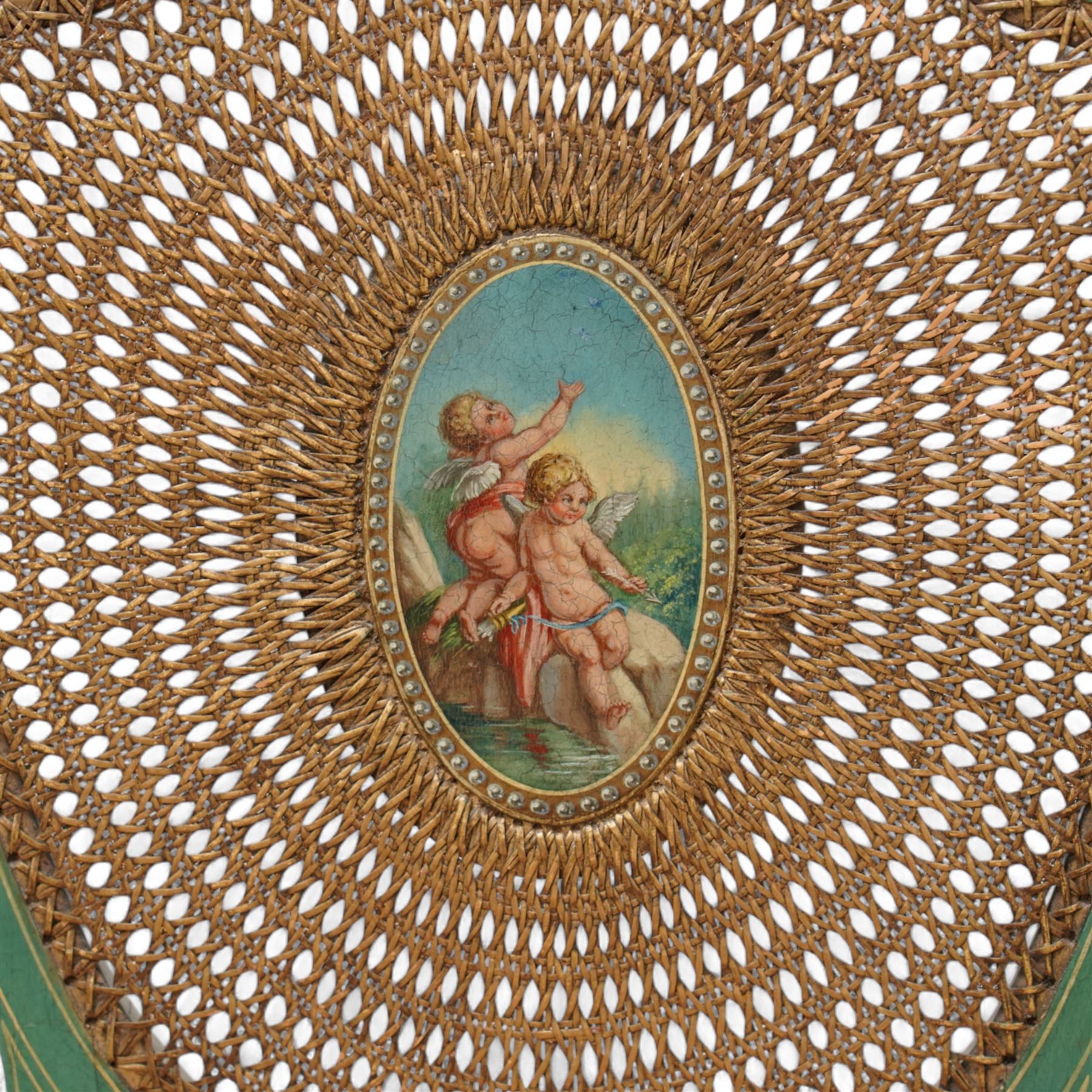 Pair of Edwardian Hepplewhite Revival green-painted open armchairs, cane work shield back with central oval panel panted with putto set upon rocky landscape with water and trees, shaped and rolled arms enclosing cane work seat, on turned front supports decorated with acanthus leaves and draped festoons 