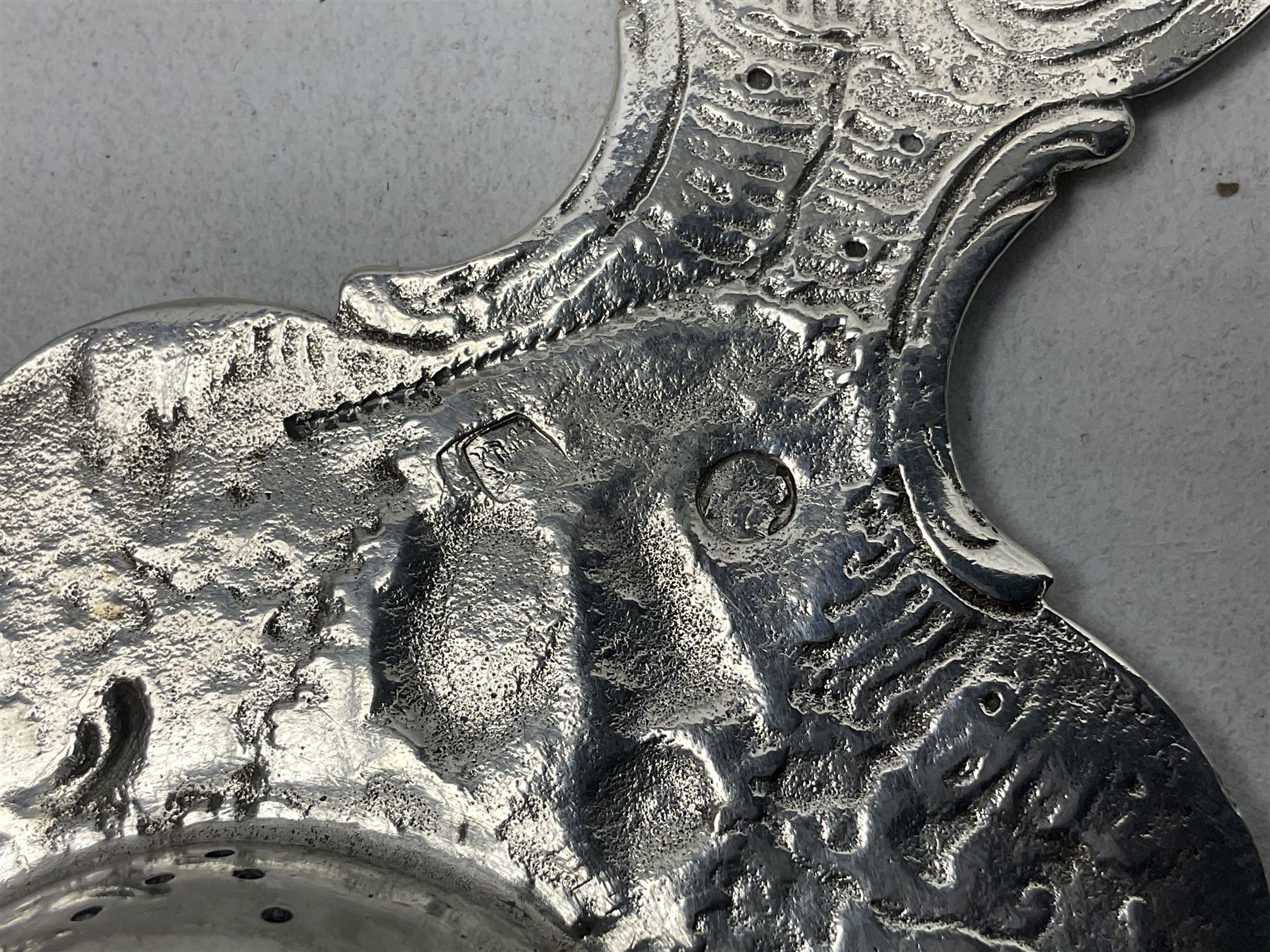 Continental white metal strainer, of shaped form embossed with classical figures, putto, musical trophies and fruiting vines, indistinctly marked, L12.5cm