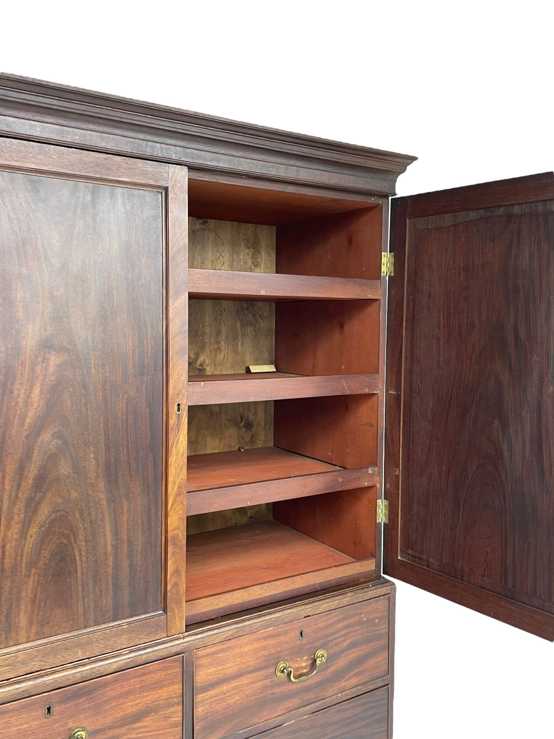 George III mahogany Gentleman's linen press, the projecting cornice over two panelled cupboard doors enclosing three sliding trays, the base fitted with two short over three long graduating cock-beaded drawers, lower moulded edge over bracket feet