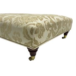 Large rectangular footstool, upholstered in cream self-embossed fabric on turned mahogany feet with brass cups and castors