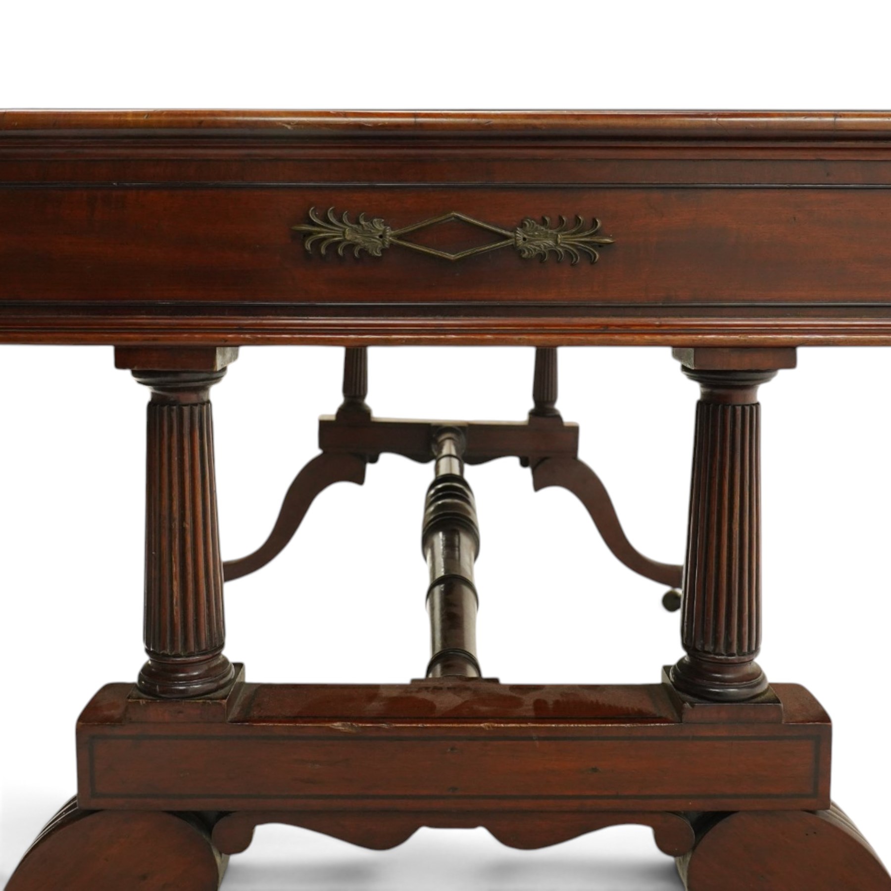Regency inlaid mahogany and brass mounted library table, the rectangular top inset with gilt tooled burgundy leather writing surface, enclosed by  crossbanding and boxwood stringing with roundel corner motifs, above three cock-beaded frieze drawers to either side fitted with brass ring handles and brass escutcheons, the end friezes centred by applied brass foliate mounts, raised on twin reeded column supports over rectangular platform ends, united by a ring-turned stretcher, the reeded sabre legs terminating in brass caps and castors, one drawer bearing ivorine label 'Spillman & Co., St Martins Lane, London'