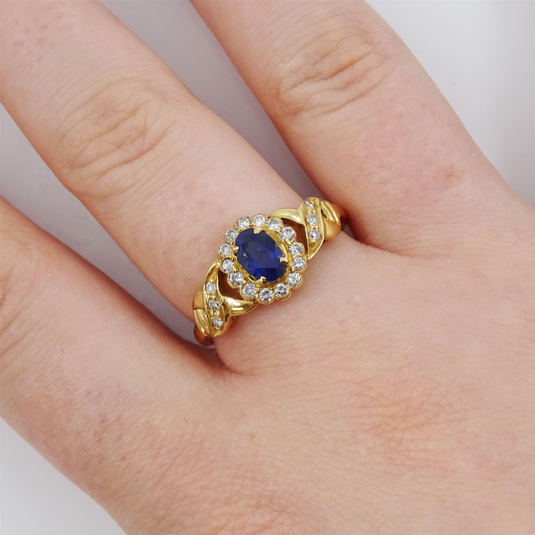 18ct gold sapphire and diamond cluster ring, single oval cut sapphire of approx 0.50 carat, surrounded by fourteen round brilliant cut diamonds, with pierced crossover diamond set shoulders, stamped, total diamond weight approx 0.20 carat
