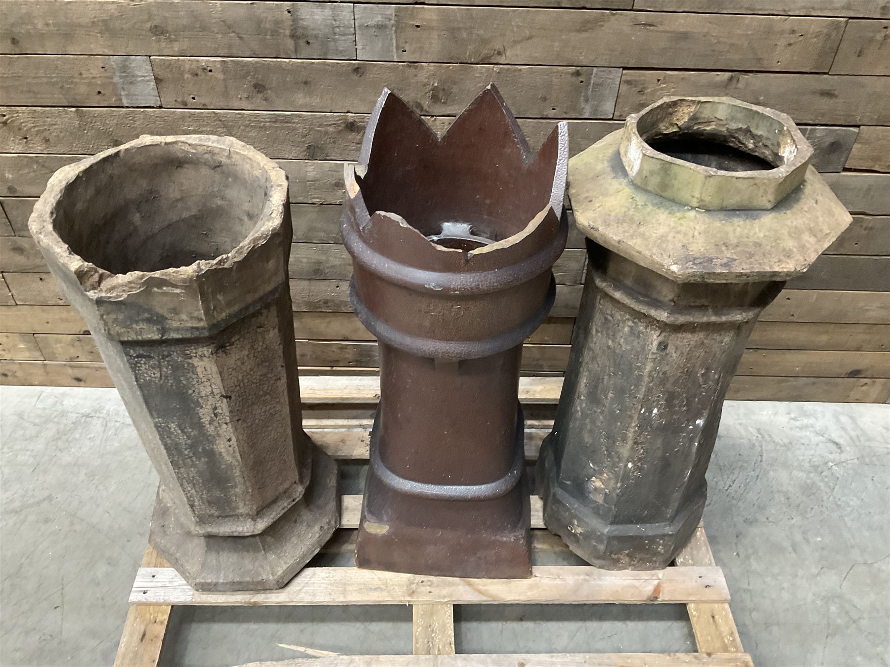 Collection of three Victorian and early 20th century reclaimed terracotta chimney pots, comprising: one cylindrical form with weathered, cracked glaze and flared octagonal base; one deep red cylindrical pot with fluted midsection and castellated rim, bearing moulded number ‘25’; and one tapering hexagonal example with wide flared rim and weathered patina. All with age-related wear and chips, consistent with use and outdoor exposure. Plus a selection of cast stone pieces including fountain 