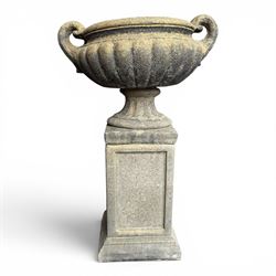 Pair of Neoclassical design weathered cast stone garden urns of kylix form, the rolled rim flanked by twin pierced scroll handles over a shallow gadrooned bowl, raised on a fluted circular socle and faux panelled square pedestal base