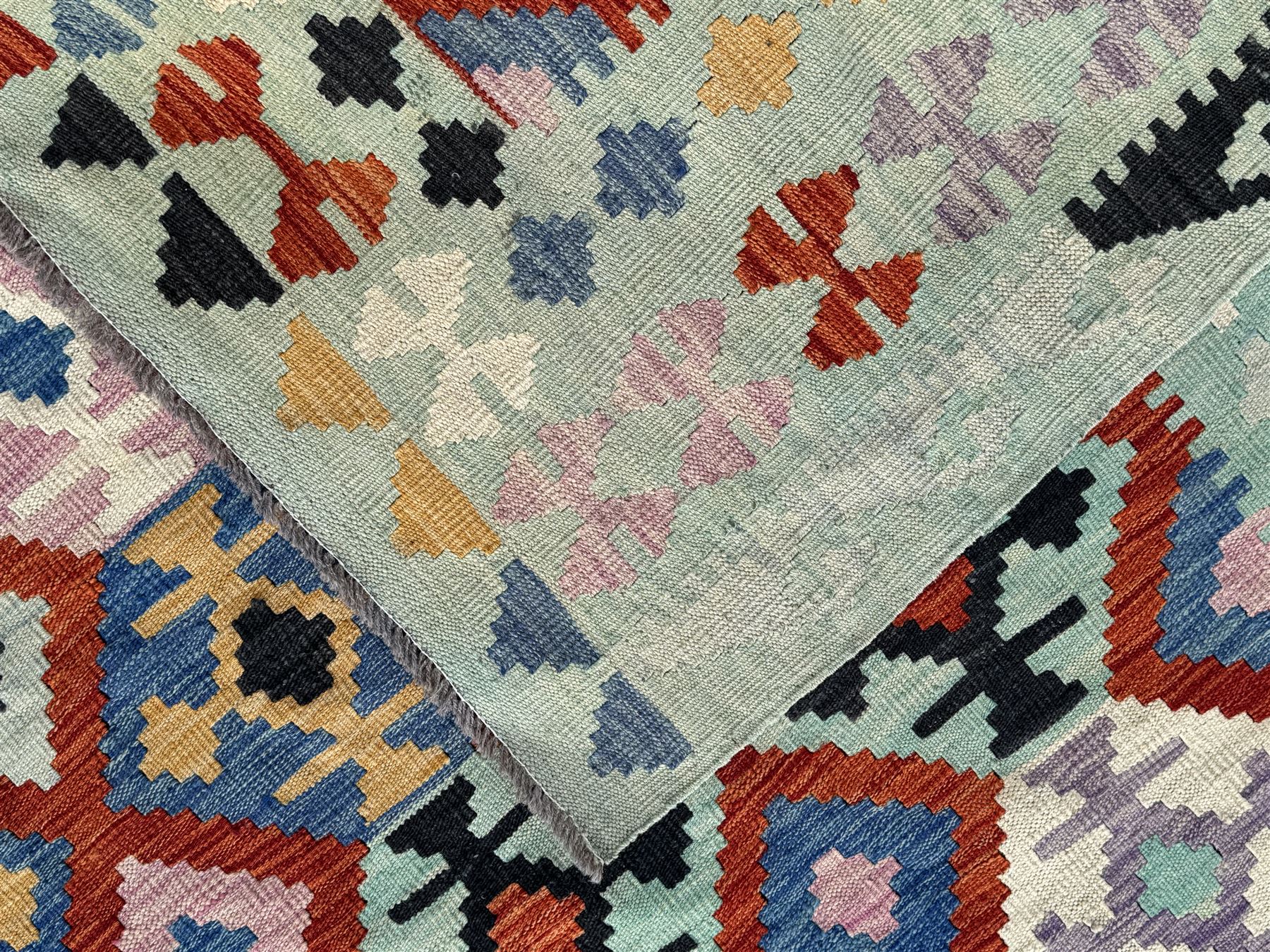 Kilim pastel ground rug, the field decorated with repeating multicoloured geometric diamond motifs, enclosed within matching geometric borders