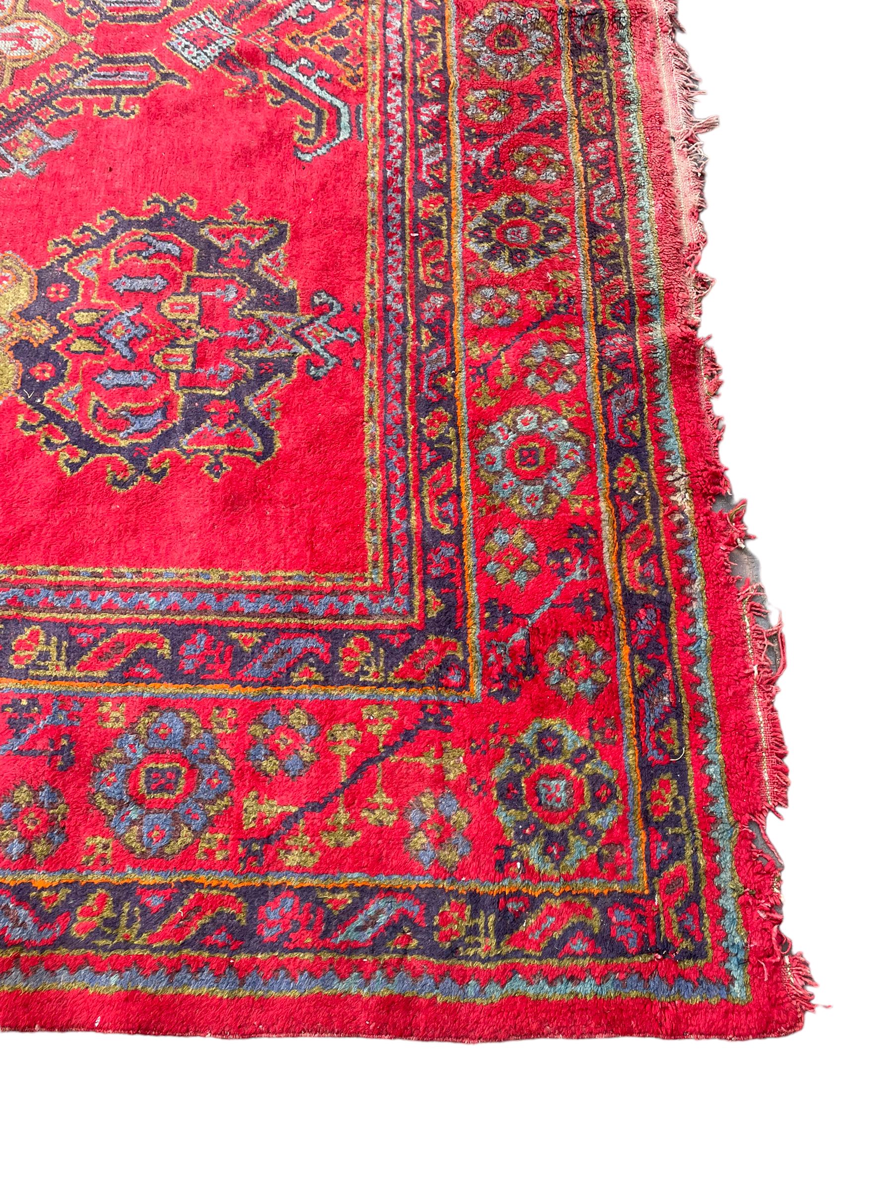 Early 20th century Western Anatolia Turkish Oushak crimson ground carpet, the field decorated with rows of Herati and Palmette medallions, the main border decorated with stylised flower head motifs within guard stripes