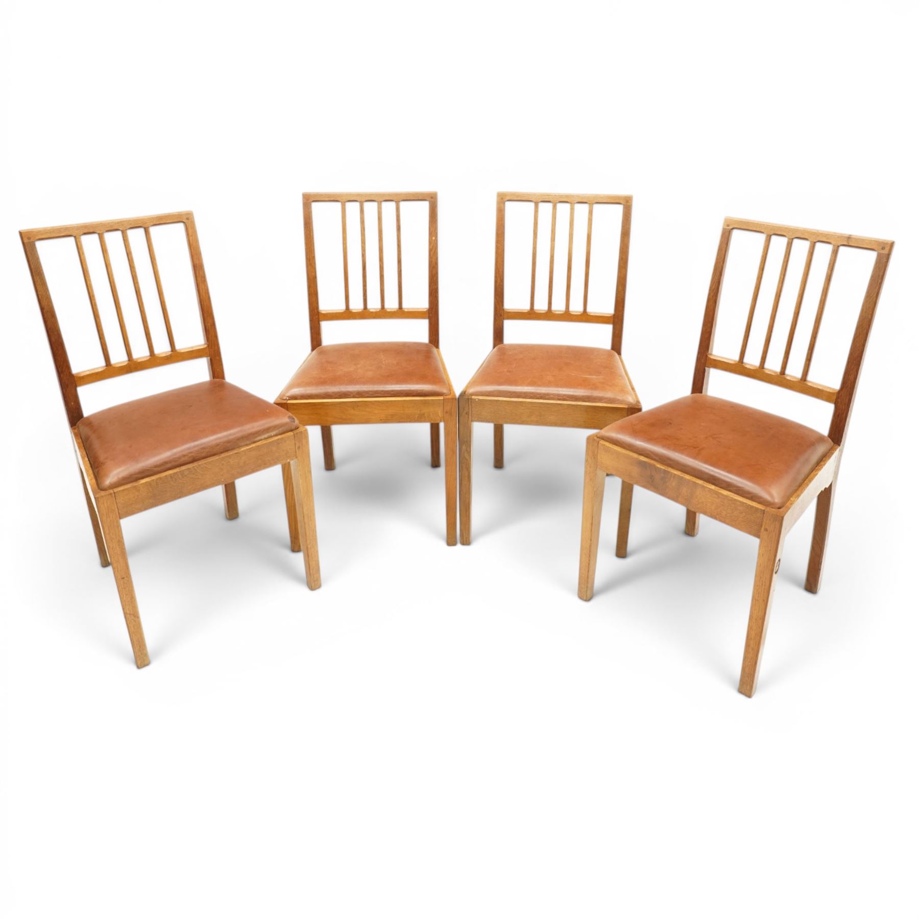 Acornman - set of four oak dining chairs, chamfered slatted back, tan leather drop in seat, raised on square supports with carved acorn signature, by the workshop of Alan Grainger of Brandsby