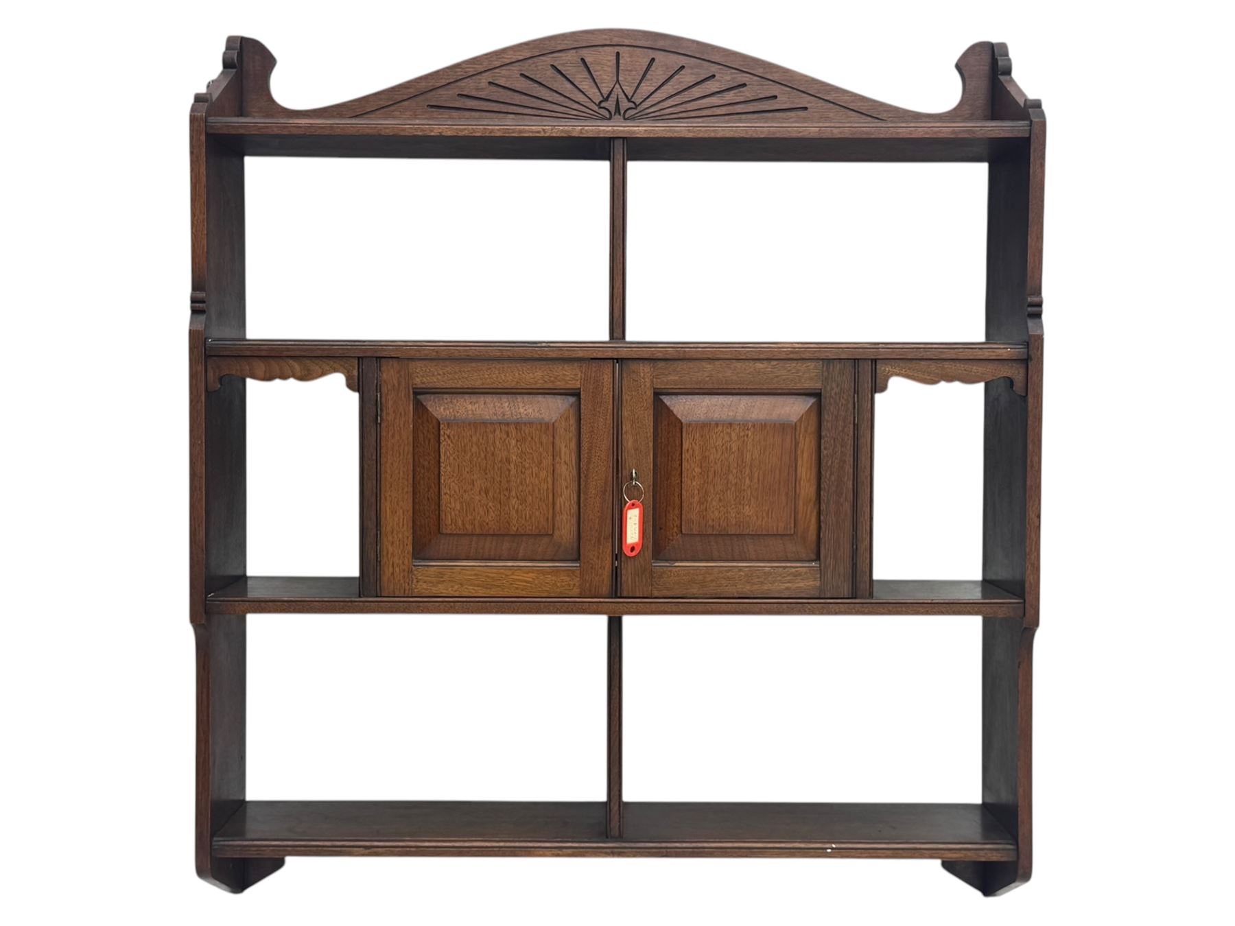 20th century carved mahogany hanging wall shelf, shaped top rail with carved fan motif over central twin cupboard flanked by fixed shelves, open base with three-tier shelving