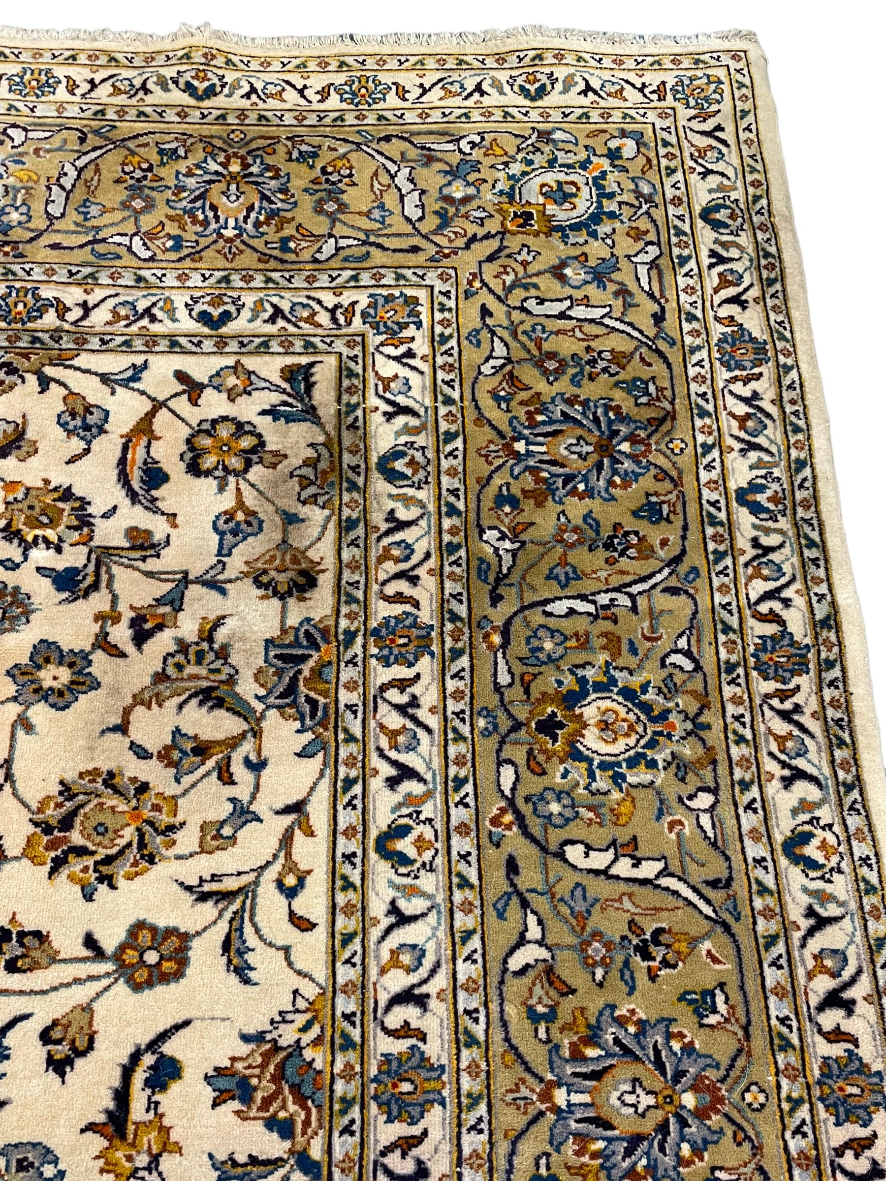 Persian Kashan ivory ground carpet, the field decorated with trailing foliate branches and stylised flower head motifs, guarded border with repeating design decorated with scrolling leafy branch and plant motifs 