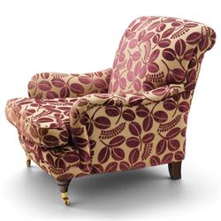Traditional Howard shape armchair, rolled back and arms over deep seat, raised on turned supports with brass cups and castors, upholstered in plum foliate patterned fabric with loose seat cushion