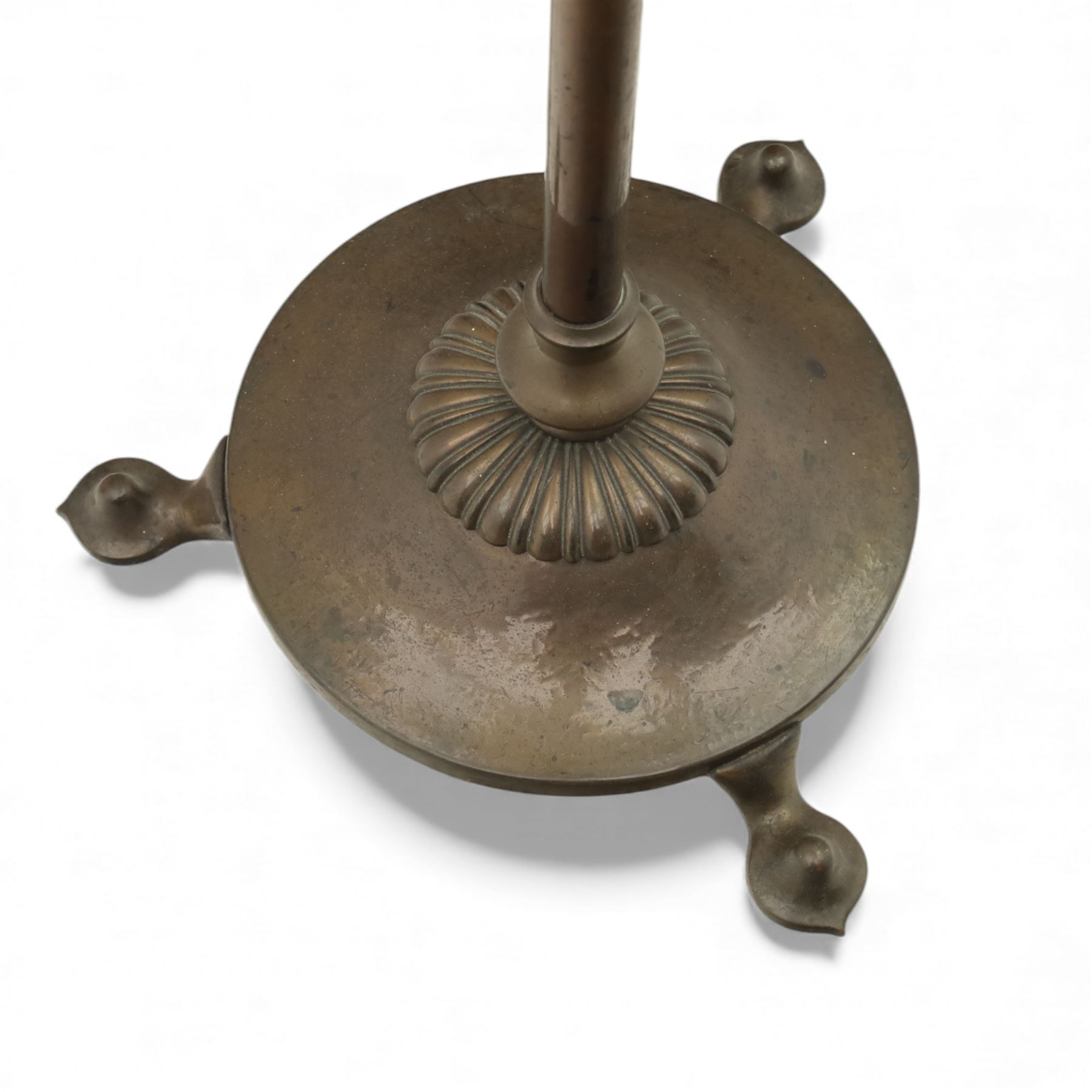 Early 20th century Art Nouveau metal standard lamp, the slender column with adjustable collar, raised on a circular dished base with three pad feet, fitted with a metal gallery and bulb holder, beige raw hide with fringe 