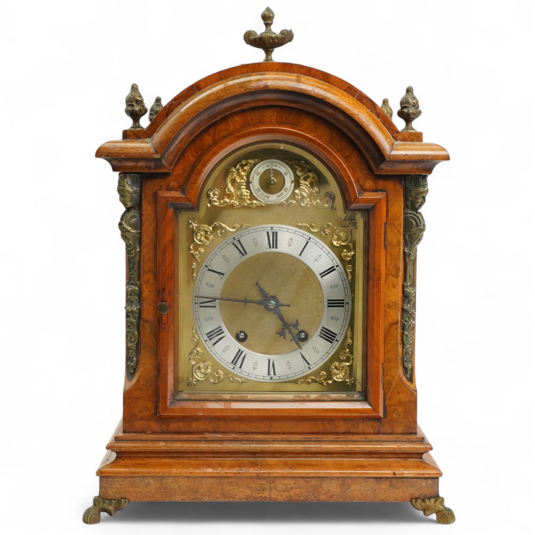 German-early 20th century mantle clock c1910, in a walnut case with a break arch top and decorative cast brass finials, brass silk backed sound frets to the sides and a glazed break-arch door flanked by a pair of cast brass caryatid, on a dee ogee moulded plinth and raised on splayed paw feet, brass dial with cast spandrels and a matted dial centre, silvered chapter ring with Roman numerals, gothic steel hands and a conforming pendulum regulation dial to the arch, two train going barrel movement with rack striking, sounding the quarters on two gongs and the hour on one, With Pendulum and key.
