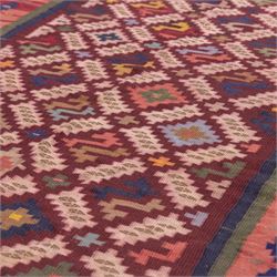 South West Persian Qashgai flatweave kilim, field decorated with a repeating diagonal lattice of stepped lozenges and angular hooked motifs, interspersed with small tribal devices, woven is shade of madder red, soft pink, indigo blue, ochre, and olive green, framed by a narrow geometric border and contrasting guard stripes 