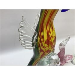 Three Murano style glass cockatoo parrots, the first with mottled yellow, red and orange body, clear outstretched wings, dark blue beak and red crest, raised upon clear stylised base, the second smaller parrot with merging blue and green body, and further with pink striped body, tallest H40cm