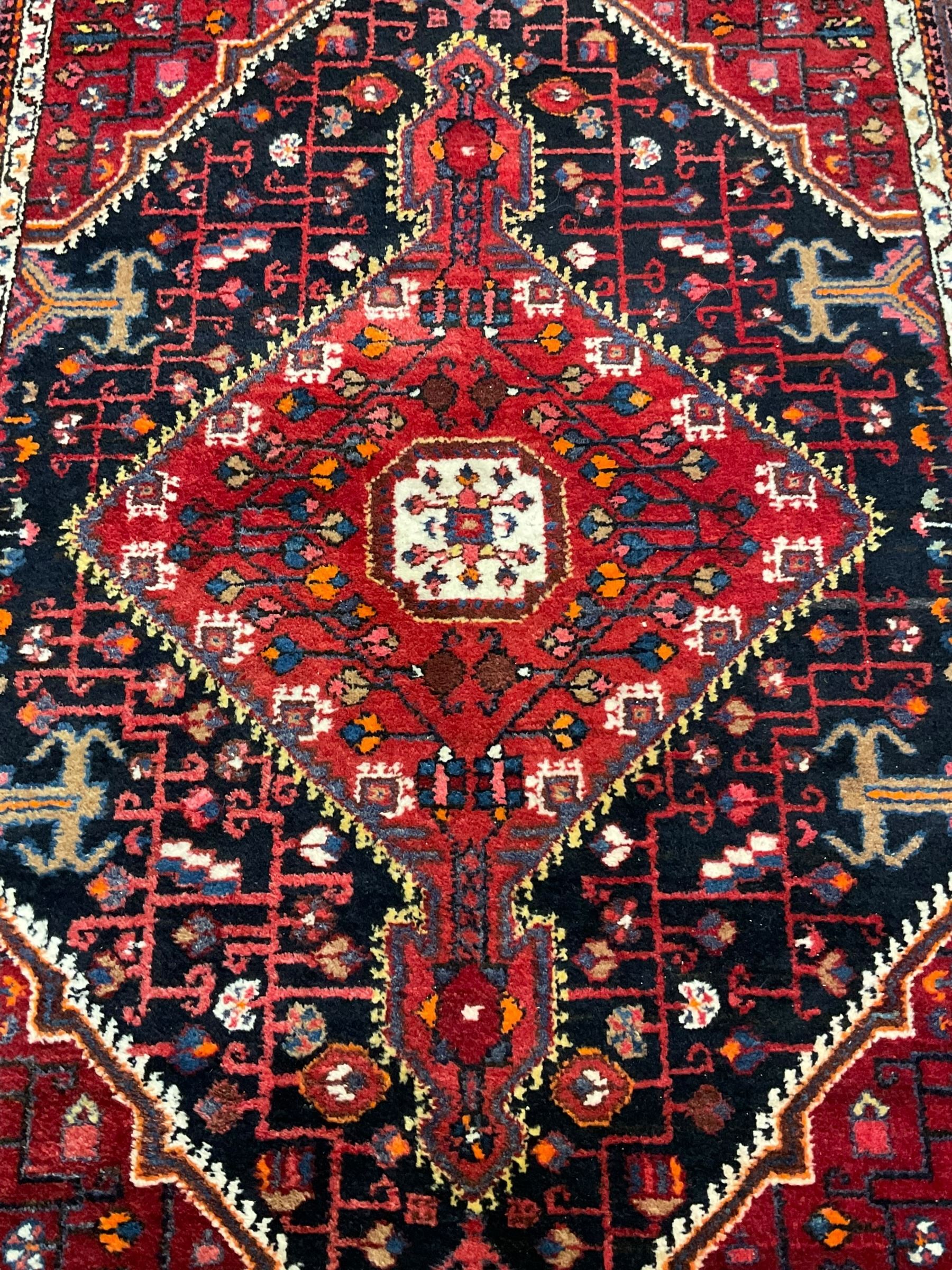 Persian Hamadan red and indigo ground rug, central lozenge medallion with extending poles, the field decorated with interlaced branches and flowerheads, guarded border with stylised floral motifs