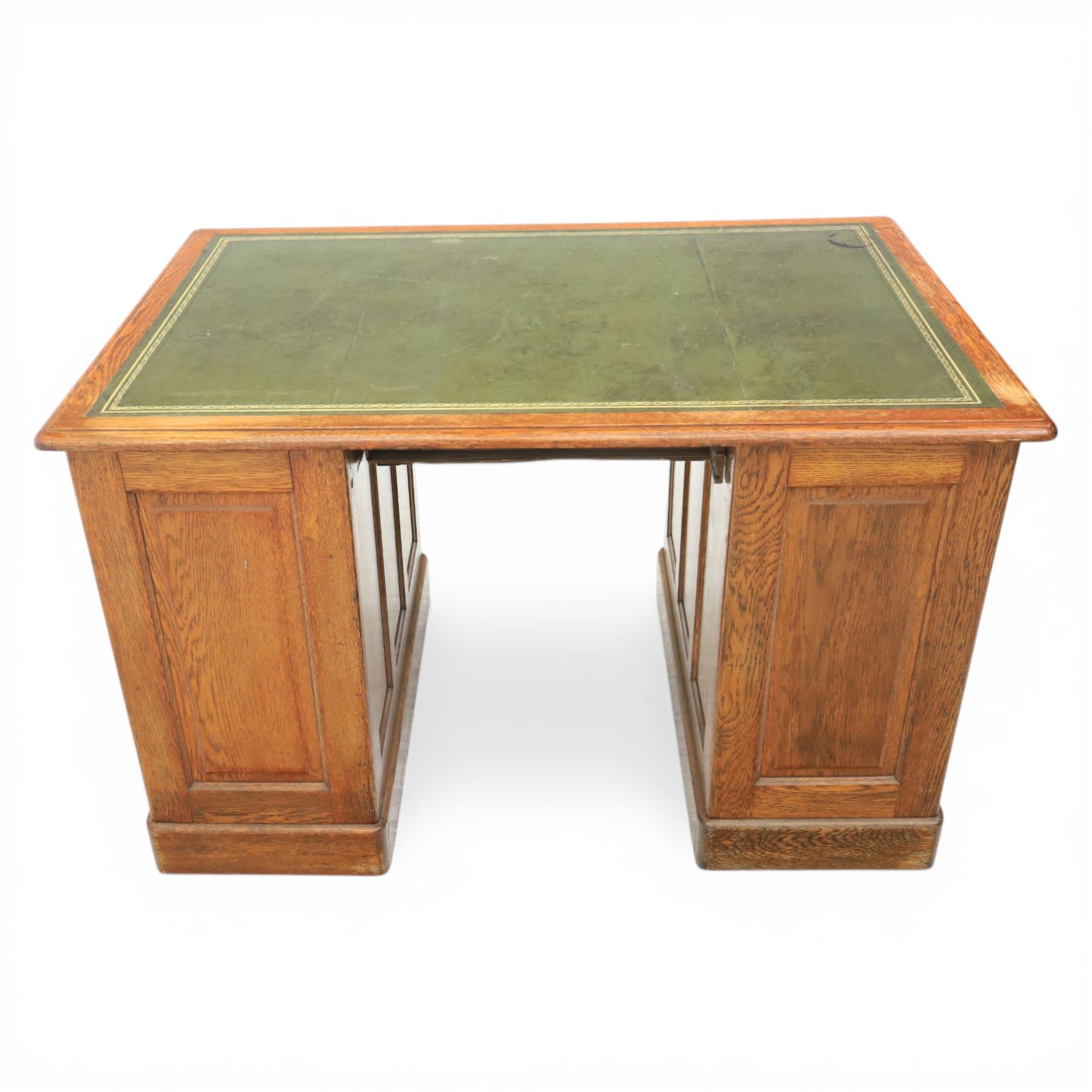 20th century oak compact pedestal desk, tooled green leather inset top, above a single frieze drawer, with a bank of four graduated drawers and a drawer and cupboard, panelled sides raised on castors