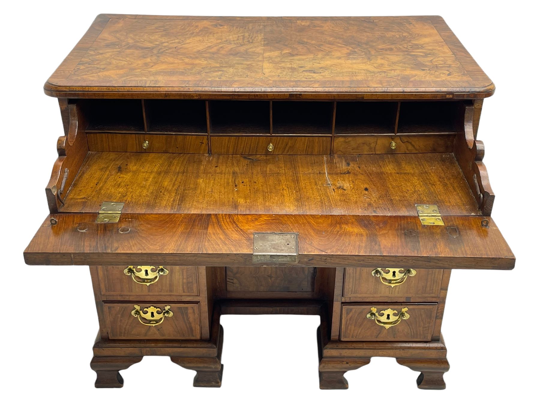 Early 18th century Queen Anne figured walnut kneehole desk with secretaire drawer, moulded and book matched top with walnut band, the top drawer with fall front enclosing small drawers and pigeon holes, fitted with nine drawers and central recessed cupboard, on ogee bracket feet