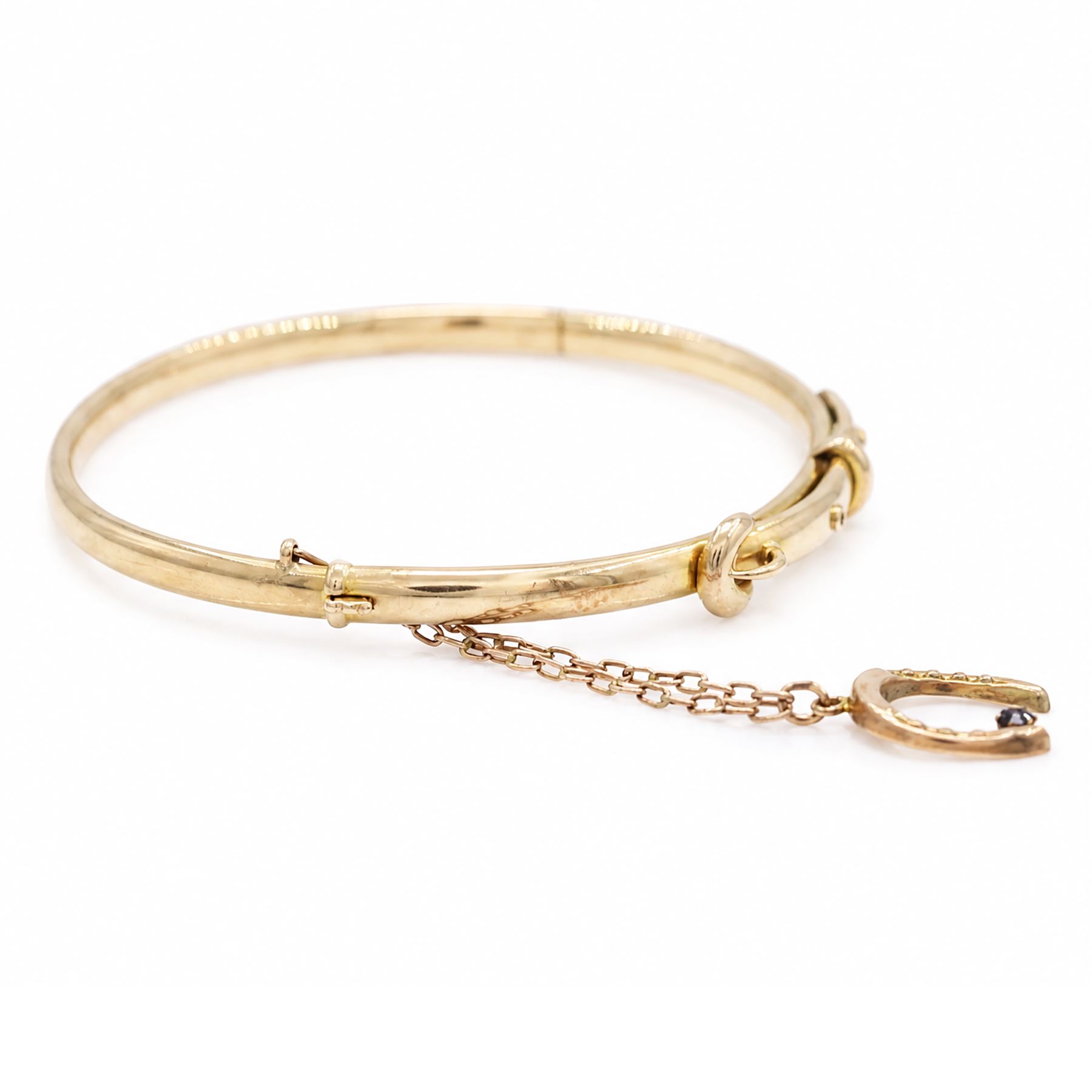 Early 20th century 15ct gold buckle hinged bangle, stamped 15, the safety chain with a 9ct rose gold horseshoe charm, set with a single sapphire