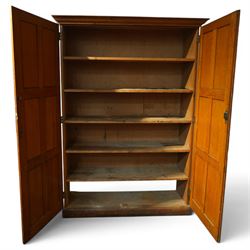 Early 20th century Arts and Crafts oak housekeeper’s cupboard, moulded cornice above pair of panelled doors enclosing a shelved interior, on plinth base