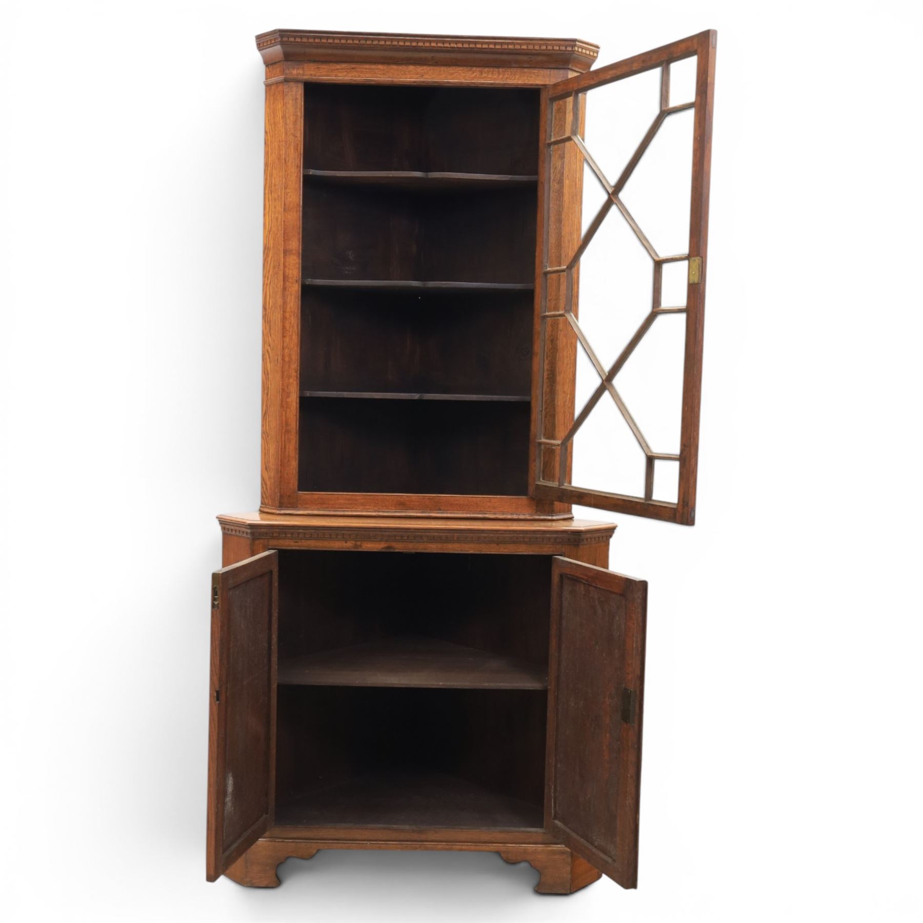 19th century oak floor-standing corner display cabinet, dentil cornice above astragal glass, shaped fixed shelves, the lower section with twin cupboard doors, on shaped bracket feet