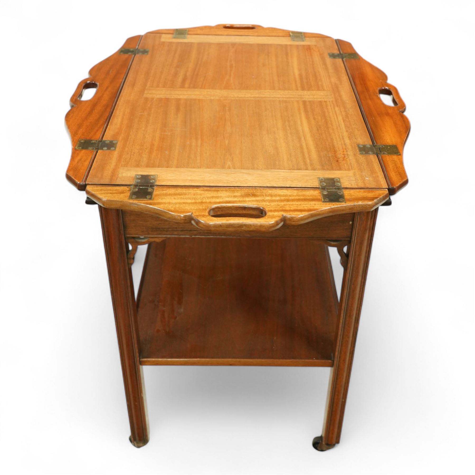 20th century mahogany butler’s tray on stand, with folding gallery tray top featuring shaped hand grips and brass hinges, fitted with single drawer and lower shelf, on square section legs with pierced brackets and castors