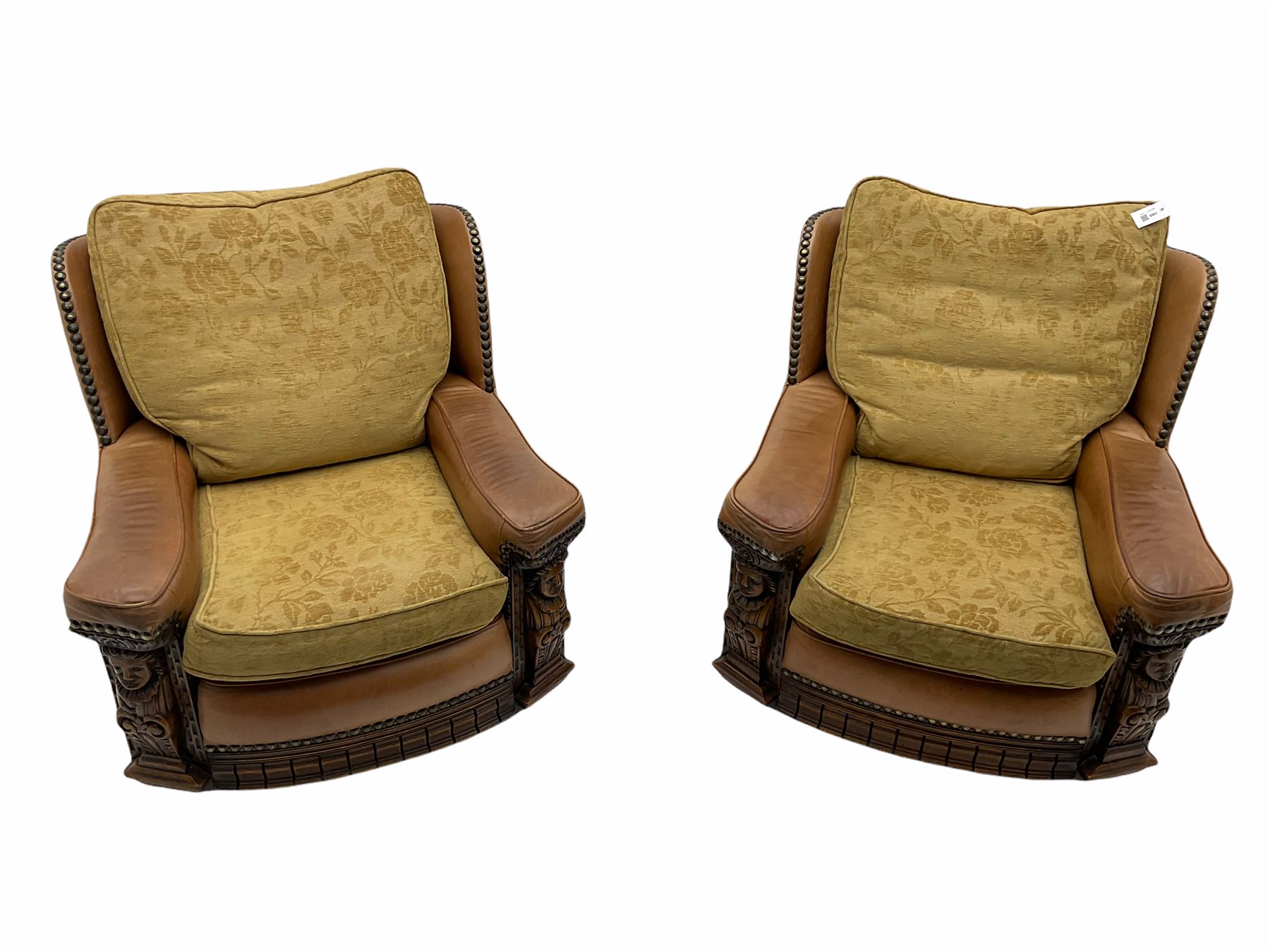 Pair of 1930’s carved oak framed club chairs, upholstered in tan studded leather with beige fabric loose cushions