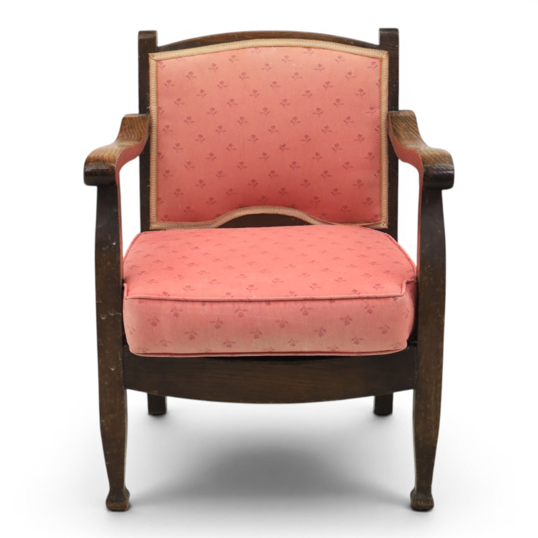 Early 20th century small oak open armchair, arched upholstered back with brass stud border over shaped seat cushion upholstered in pink foliate fabric, shaped open arms on square supports