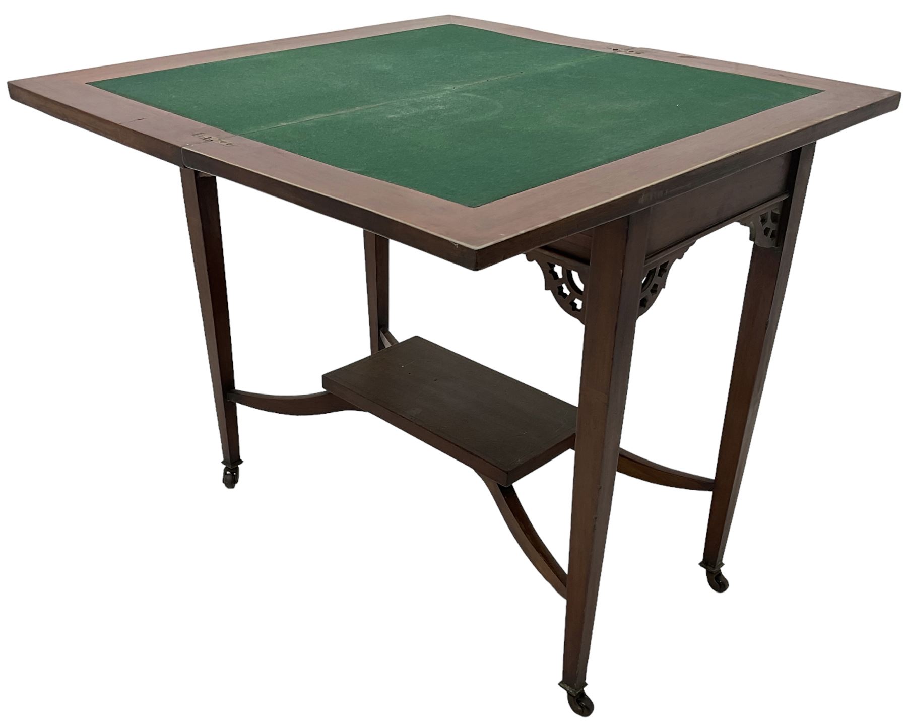 Edwardian inlaid mahogany games table, the rectangular fold-over swivel top decorated with central shell motif inlay and ebony stringing, raised on tapering supports united by shaped X-stretcher and undertier