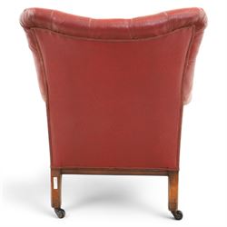 Early 20th century style oxblood red leather Chesterfield armchair, deep buttoned shaped back over padded scroll arms and loose seat cushion, raised on turned mahogany front supports with brass caps and castors
