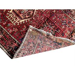 Persian Karajeh crimson ground runner rug, the field set with seven geometric lozenge medallions, the field decorated all over with stylised plant motifs, the banded border with repeating geometric shapes and patterns