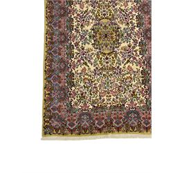 Central Persian Kirman ivory ground rug, decorated all-over with flower heads and trailing foliage, shaped pink and blue ground borders with olive green outer band