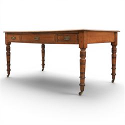 Victorian pitch pine writing table with leather inset top, rectangular top with three frieze drawers, pierced brass handles, raised on turned and fluted supports terminating in castors