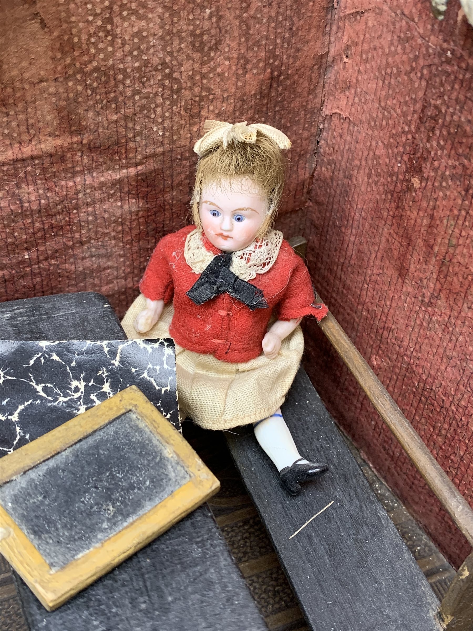 Late Victorian wooden school room setting with bisque head teacher and six German all bisque pupils each seated at a combined desk and chair with slate board, in a classroom furnished with chest of drawers, fire-surround, lectern, wall map, pictures, miniature books, school bell, chalk board on easel, wall clock etc, L70cm H28cm D28cm