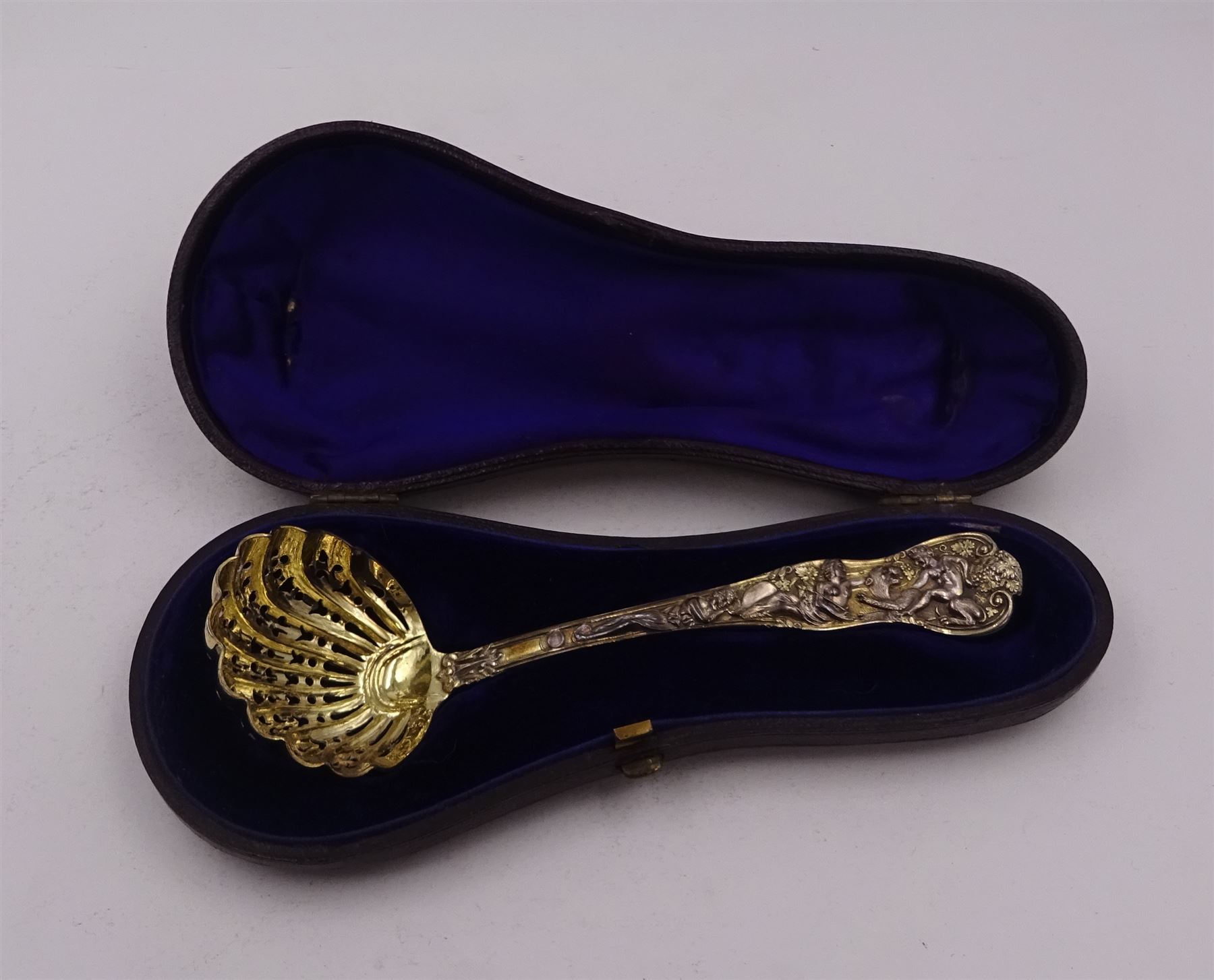 Victorian silver-gilt sugar sifting spoon, with gilded pierced shell shaped bowl, the handle decorated in relief with classical greek figures amongst fruiting vines, hallmarked Henry John Lias & James Wakely, London 1874,  L16cm, contained within tooled leather silk and velvet lined fitted case