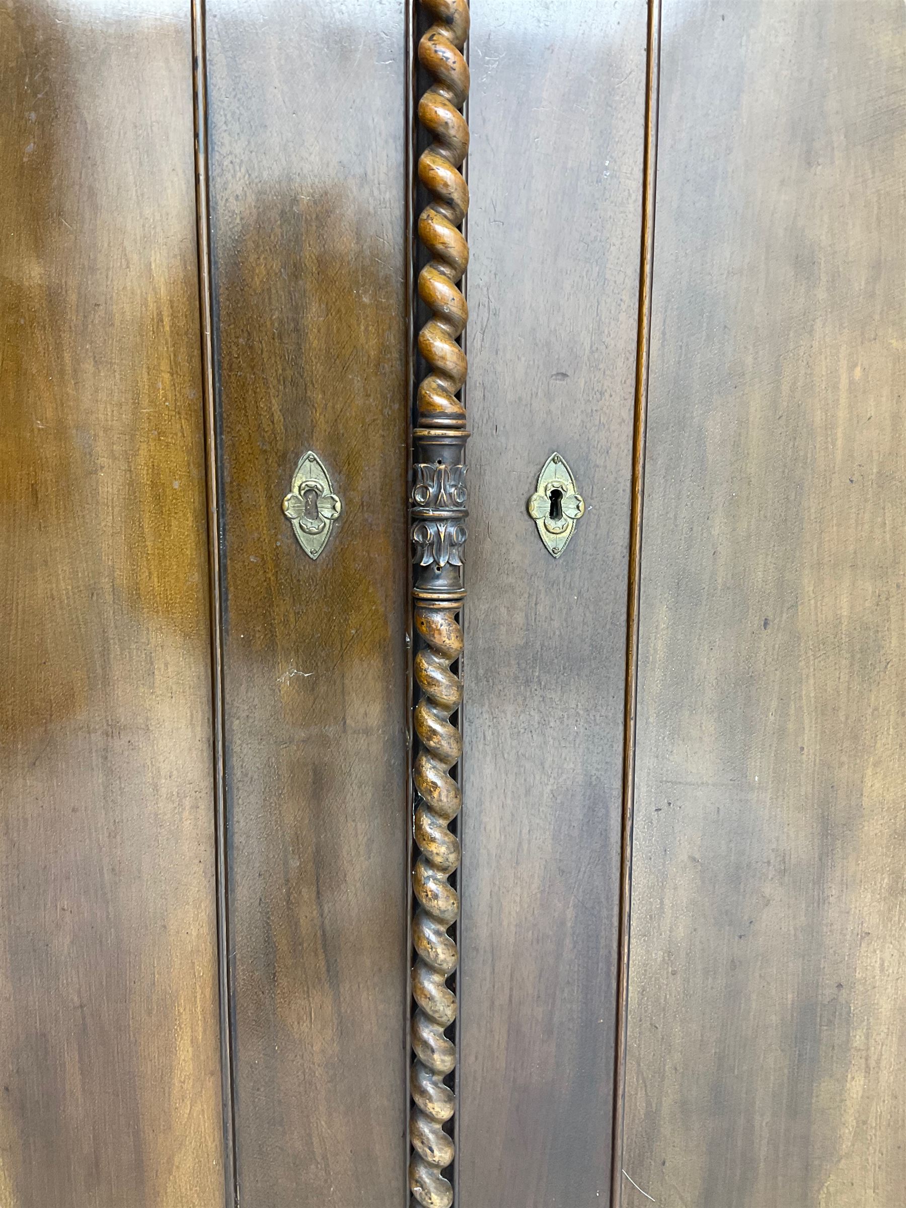 Early 20th century Italian walnut armoire wardrobe, the pierced and scrolling pediment carved with acanthus leaf detail, flanked by two scrolling cartouche with matching corbels below, the two panelled doors with applied carved rinceaux slips, with a central spiral turned upright, enclosing single shelf and hooks, raised on scroll feet